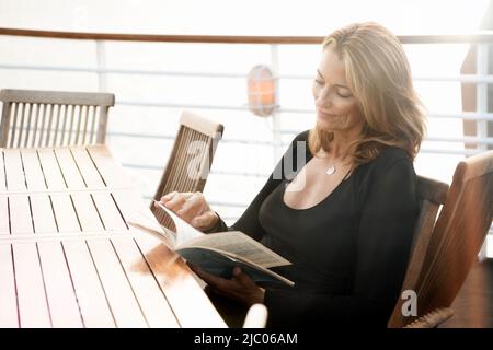 Equateur, Îles Galapagos, femme lisant le magazine tout en étant assise à table sur le pont du navire de croisière Banque D'Images