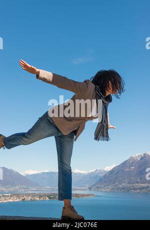 Ith Arms s'étirent et se dressaient sur une jambe et profitez de la vue panoramique sur le lac alpin majeur avec la montagne enneigée à Ascona, en Suisse. Banque D'Images