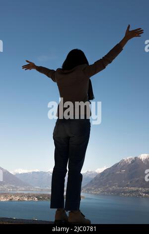 Femme aux armes s'étire et profiter de la vue panoramique sur le lac alpin majeur avec la montagne enneigée à Ascona, Suisse. Banque D'Images