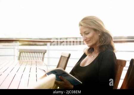 Equateur, Îles Galapagos, femme lisant le magazine tout en étant assise à table sur le pont du navire de croisière Banque D'Images