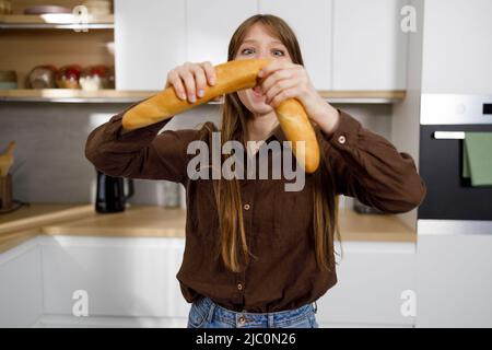 Femme affamée cassant de la baguette fraîche dans la cuisine Banque D'Images