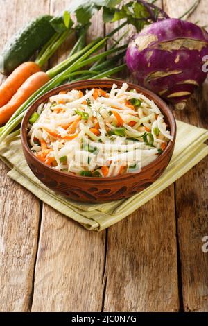 Salade de légumes préparée à partir de chou-rave, carottes, concombres et oignons verts dans une assiette sur une table en bois. Verticale Banque D'Images