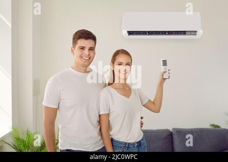 Un jeune couple heureux utilise une télécommande pour régler sa climatisation à la maison Banque D'Images