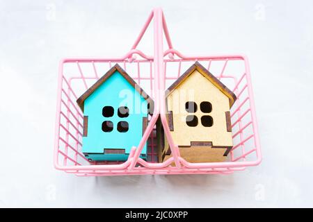 Deux modèles de maison en bois de jouet dans un panier rose sur un fond neutre. Concept de shopping à domicile. Banque D'Images