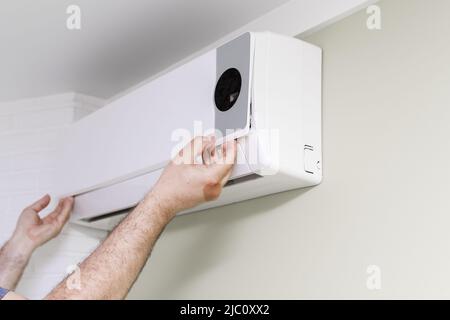 un homme retire le couvercle du climatiseur pour les réparations. les mains en gros plan Banque D'Images