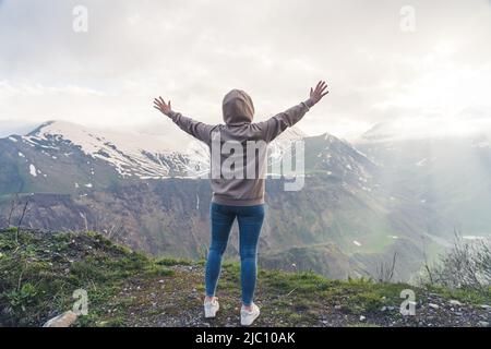 Personne méconnue dans un sweat à capuche gris et un Jean bleu écartant les bras tout en se tenant debout dans la montagne. Belle vue sur la montagne. Photo de haute qualité Banque D'Images