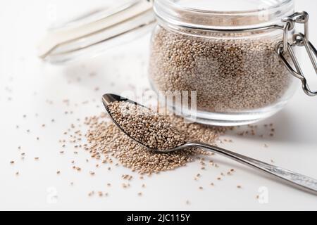 Contenant en verre avec cuillère et graines de chia blanc placées sur fond blanc. Gros plan. Banque D'Images