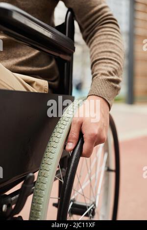 Gros plan d'un homme handicapé méconnaissable assis dans un fauteuil roulant manuel et tournant le rebord de la main en avanisant dans la rue Banque D'Images