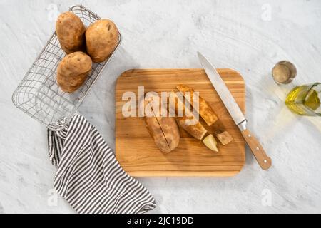 Pose à plat. Couper les pommes de terre en morceaux sur la planche à découper en bois pour les cuire au four. Banque D'Images
