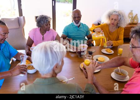 Vue en grand angle des amis seniors multiraciaux prenant le petit déjeuner sur la table à manger dans la maison de retraite Banque D'Images