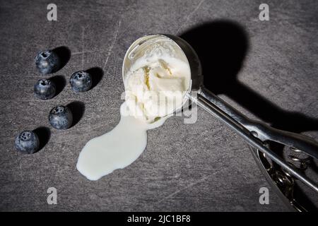 Cuillère pour la crème glacée avec la glace fondue et les bleuets sur fond sombre. Ombres dures et spectaculaires. Concept de scène de crime Banque D'Images