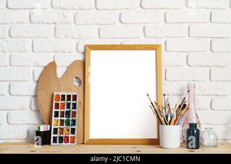 Cadre photo comme chevalet avec les outils de l'artiste sur une table en bois contre un mur en brique blanche Banque D'Images