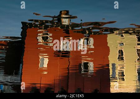 Distorsions de rêve dans un reflet inversé dans le port du petit port nord du lac de Garde de Torbole sul Garda, Trentin-Haut-Adige, Italie, de bâtiments de front de mer peints en rouge foncé et vert clair. Banque D'Images