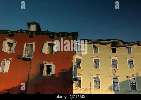 Torbole sul Garda, Trentin-Haut-Adige, Italie: La surface toujours mobile du Lago di Garda crée des distorsions oniriques dans cette image inversée de bâtiments rouge foncé et vert clair reflétés dans le petit port de cet ancien port frontière près de la pointe nord du lac. Banque D'Images