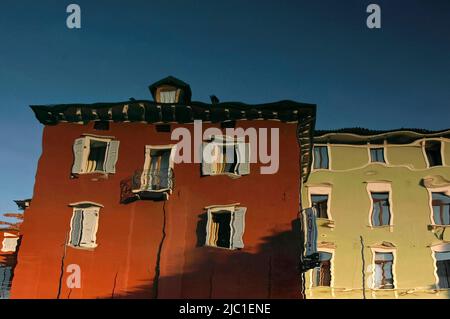 Le côté surréel du lac de Garde ... des lignes ondulées et des fenêtres wonky dans un reflet inversé dans le port au petit port nord de Torbole sul Garda, Trentin-Haut-Adige, Italie, des bâtiments de front de mer peints en rouge foncé et vert clair. Banque D'Images