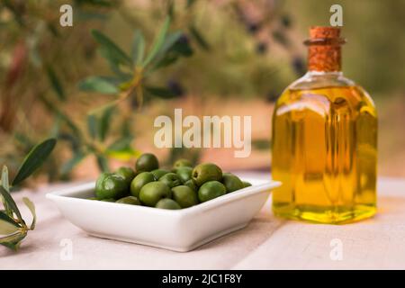 olives vertes mûres, huile d'olive dans un verre bouteille traditionnelle sur une table dans un jardin d'oliviers Banque D'Images