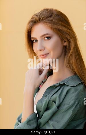 femme souriante et rouge en chemise de lin vert posant près du mur beige Banque D'Images