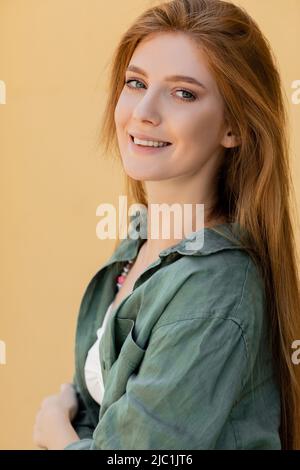 femme heureuse et rouge en chemise de lin vert posant près du mur beige Banque D'Images