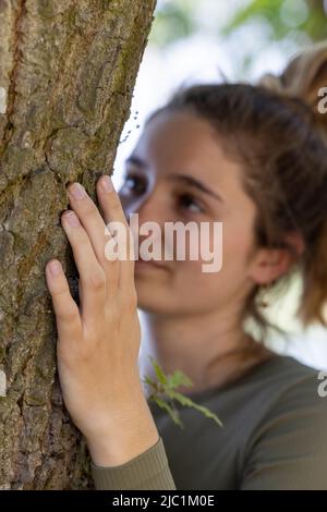 Une jeune femme contentée embrasse un grand arbre avec une expression blissful et ses yeux fermés dans un concept de sauver la forêt, d'arrêter la déforestation, le jour de la terre, en lien avec la nature et la conservation de la nature. Photo de haute qualité Banque D'Images