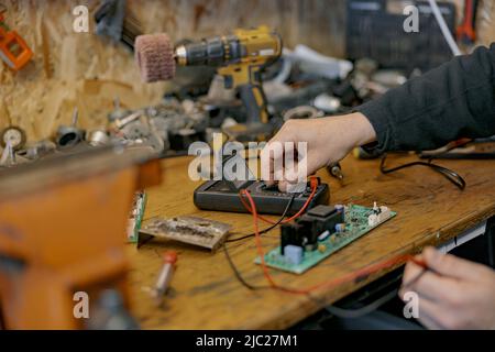 Gros plan des mains d'électricien vérifie la tension électrique sur la carte de circuit imprimé à l'aide d'un dispositif Banque D'Images