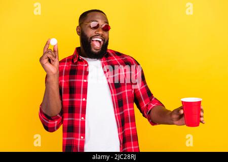 Photo de gai heureux jeune homme tenir rouge tasse bière jeu de pong isolé sur fond jaune de couleur Banque D'Images