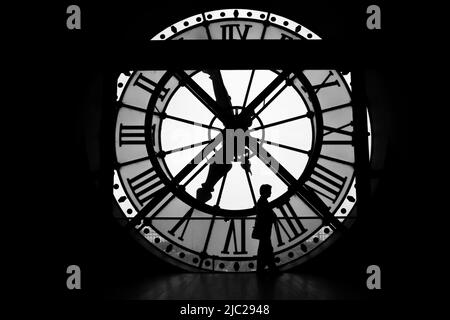 Paris, France : silhouette noire et blanche dramatique d'une femme debout immobile alors que les mains du temps se déplacent. Grand cadran d'horloge au Musée d'Orsay. Banque D'Images