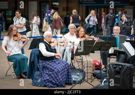 Les membres de l'Orchestre du violon écossais jouent dans une représentation pop-up à la gare Waverley d'Édimbourg, dans un court concert de musique traditionnelle de leur répertoire pour divertir les passants sur le hall avant leur prochain concert à Usher Hall samedi. Date de la photo: Jeudi 9 juin 2022. Banque D'Images