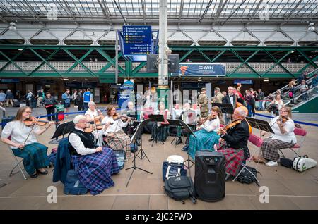 Les membres de l'Orchestre du violon écossais jouent dans une représentation pop-up à la gare Waverley d'Édimbourg, dans un court concert de musique traditionnelle de leur répertoire pour divertir les passants sur le hall avant leur prochain concert à Usher Hall samedi. Date de la photo: Jeudi 9 juin 2022. Banque D'Images