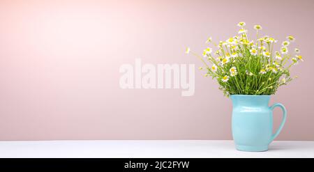 Bouquet de pâquerettes dans une carafe bleue sur fond rose Banque D'Images