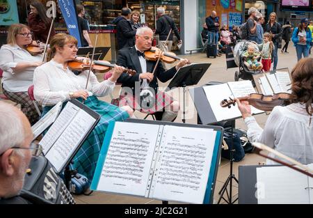 Les membres de l'Orchestre du violon écossais jouent dans une représentation pop-up à la gare Waverley d'Édimbourg, dans un court concert de musique traditionnelle de leur répertoire pour divertir les passants sur le hall avant leur prochain concert à Usher Hall samedi. Date de la photo: Jeudi 9 juin 2022. Banque D'Images