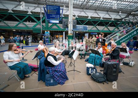 Les membres de l'Orchestre du violon écossais jouent dans une représentation pop-up à la gare Waverley d'Édimbourg, dans un court concert de musique traditionnelle de leur répertoire pour divertir les passants sur le hall avant leur prochain concert à Usher Hall samedi. Date de la photo: Jeudi 9 juin 2022. Banque D'Images