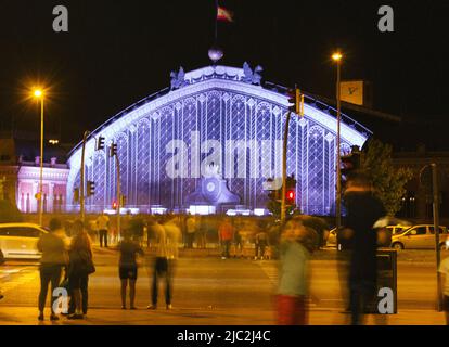 Madrid, Espagne. 2 juin 2022. Célèbre façade de la gare d'Atocha le soir, la nuit. Les piétons se tiennent à l'intersection à la lumière rouge d'un tr Banque D'Images