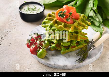 Gaufres belges vertes. Épinards ou ail sauvage ou gaufres au pesto avec saumon rouge et sauce à la crème sur fond de table en béton gris. Délicieux petit déjeuner, Banque D'Images