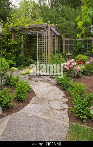 Chemin en pierre menant à la pergola dans le jardin résidentiel paysagé de cour en été. Banque D'Images