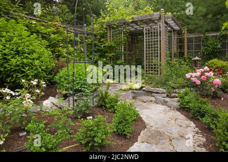 Chemin en pierre menant à la pergola dans le jardin résidentiel paysagé de cour en été. Banque D'Images