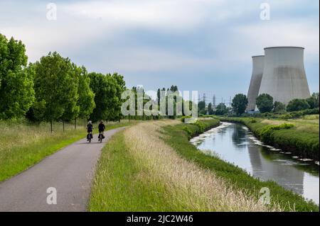 Vilvoorde, Brabant flamand, Belgique - 06 04 2022 - cycliste sur une piste cyclable au bord de la rivière Senne avec deux cheminées de centrales électriques à l'arrière Banque D'Images