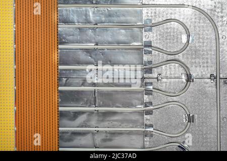 Fragment de tuyaux de chauffage au sol avec une base en aluminium et une grille métallique de protection avec isolation thermique. Banque D'Images