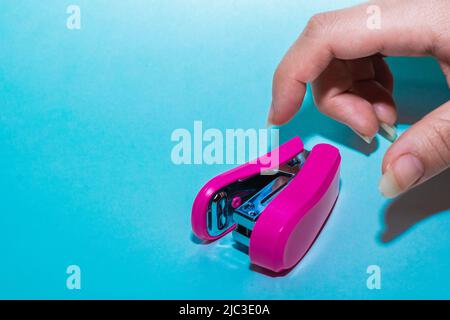 la main d'une jeune femme latine, avec de longs ongles, ouvrant ses doigts pour saisir une agrafeuse de papier sur un fond bleu. article utilisé pour le travail de bureau et fili Banque D'Images