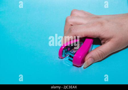 main de jeune femme latine, avec de longs ongles, tenant une agrafeuse sur fond bleu. article utilisé pour le travail de bureau et le classement des documents. papeterie c Banque D'Images