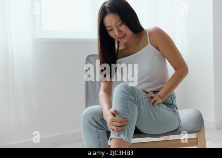 Crampes orteil cassé os cassé dans la jambe. Souffrance tourmentée bronzée belle jeune femme asiatique touche la jambe à la maison intérieur salon. Blessures faibles Banque D'Images