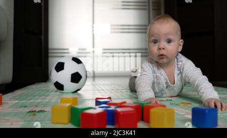 Un petit garçon joue sur le sol avec des jouets et une balle. Mignon petit garçon jouant avec des jouets sur le sol à la maison. Banque D'Images