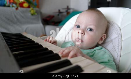 Un petit garçon est assis au clavier d'un synthétiseur. Un petit garçon s'assoit sur une chaise et apprend à jouer du piano. Banque D'Images