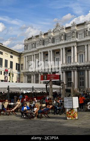 Personnes ayant des apéritifs dans un café pavé en face du Palais des Doges (Palazzo Ducale) avec les stands de la Foire du Livre à Piazza Matteotti, Gênes Banque D'Images