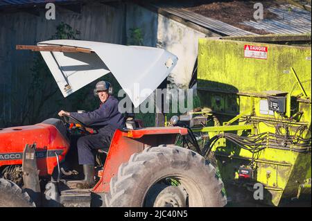 Agriculteur sur un tracteur portant des écouteurs devant un bâtiment agricole. Lower Mainland, B. C., Canada Banque D'Images