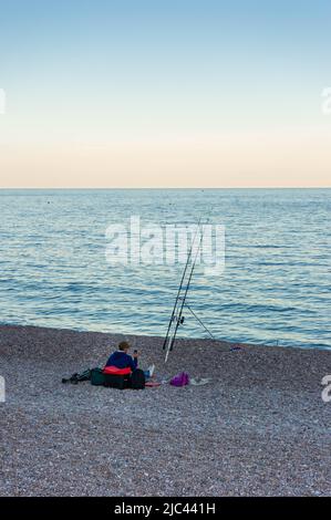 Un pêcheur solitaire sur la plage au crépuscule, Sidmouth, East Devon, Angleterre Banque D'Images