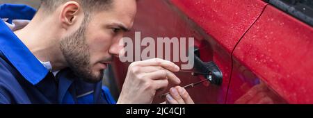 Jeune homme rouge d'ouverture de porte de voiture avec Lockpicker Banque D'Images