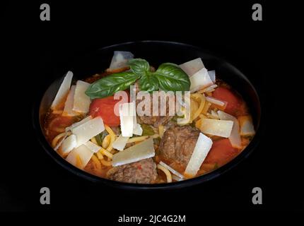 Soupe de légumes italienne minestrone, avec boulettes de veau, tomates, pecorino et spaghetti, photographie alimentaire en studio avec fond noir Banque D'Images