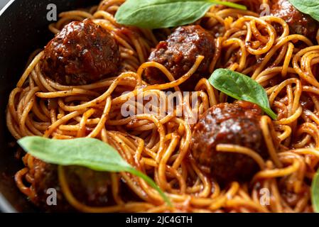 Le processus de fabrication des pâtes italiennes avec des boulettes de viande. Une assiette de spaghetti se tient à l'écart des boulettes de viande sur une plaque sur un fond sombre Banque D'Images