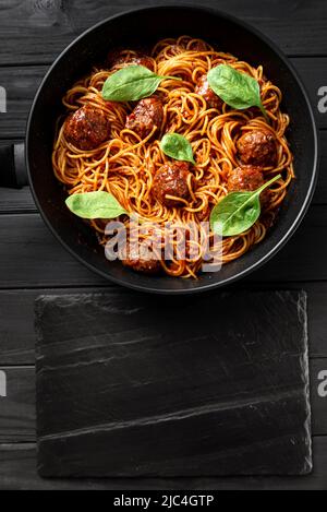 Pâtes italiennes sauce tomate avec boulettes de viande et basilic sur fond de bois foncé. Avec espace vide pour le texte Banque D'Images