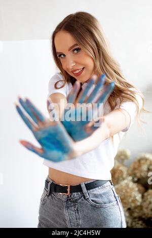 Belle blonde, sourire éclatant, jeune femme en dessin. Une femme regarde la caméra et montre des palmiers peints en bleu avec effet de flou. Banque D'Images